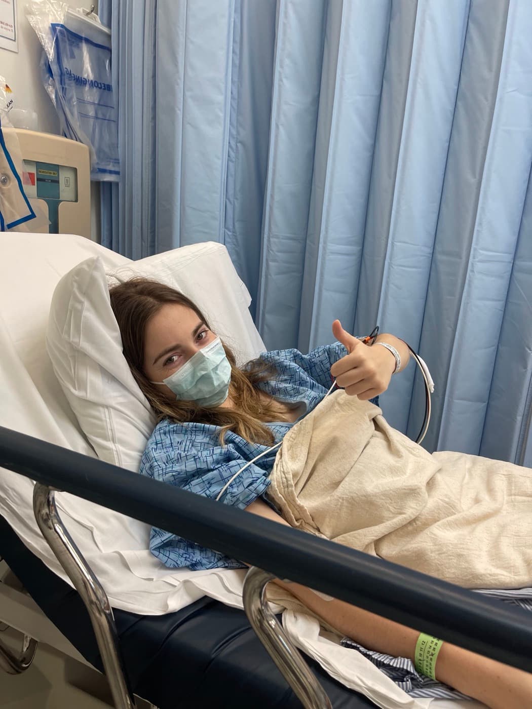 Natalia in a hospital bed during treatment, giving a thumbs up